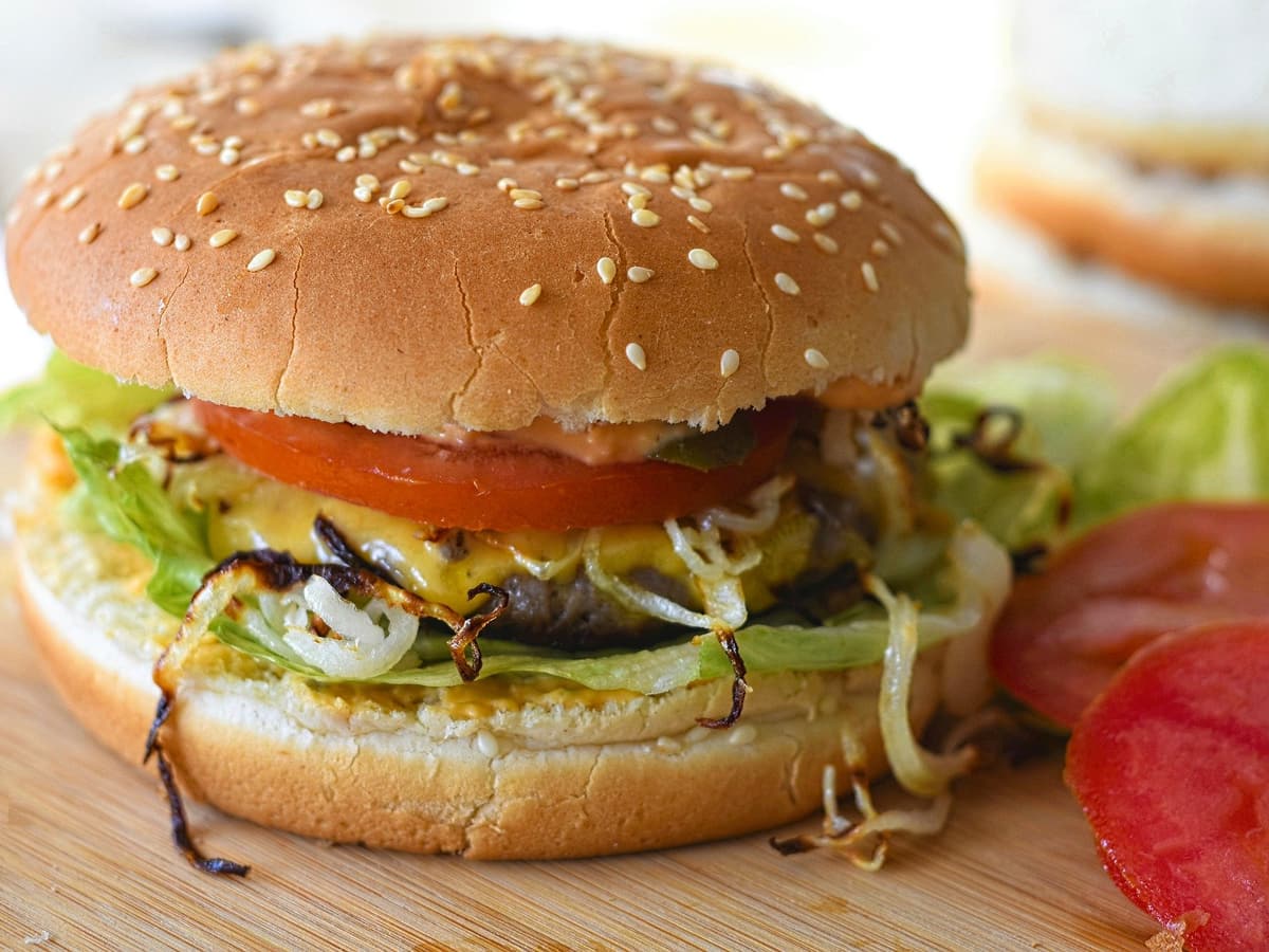 Burger mit Salat, Tomate und Zwiebeln, dahinter Pommes frites