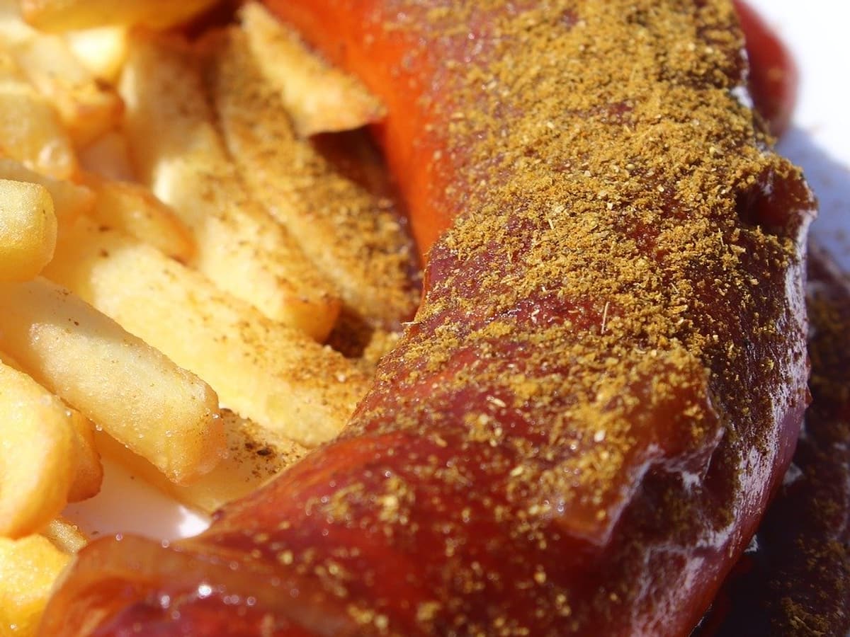 Currywurst mit Currypulver, daneben Pommes frites