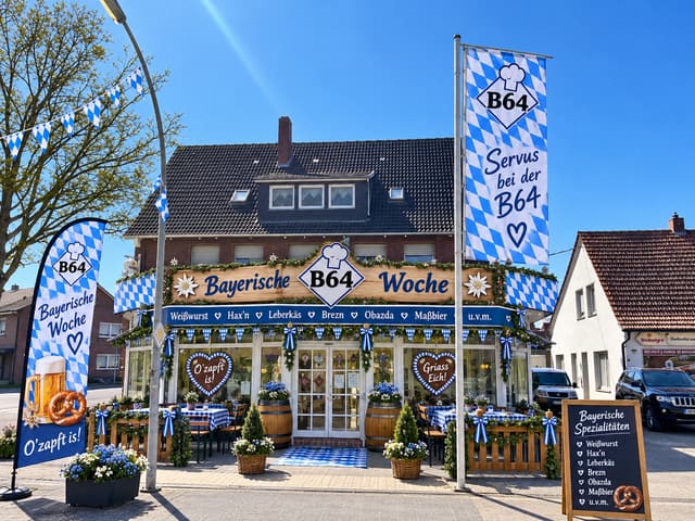 Die Grillstube zur B64 von außen, blau-weiß geschmückt zur Bayerischen Woche, mit Fahnen und Biergarnituren vor dem Eingang